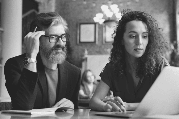 Manager (older man) working with a new hire (young woman), as they look at a laptop screen.