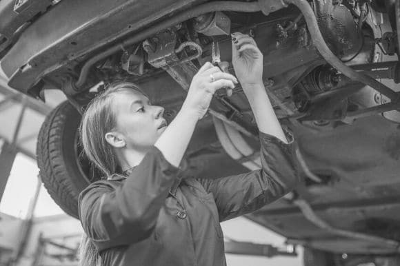 An automobile technician checks on the undercarriage of a vehicle that is up on a jack.