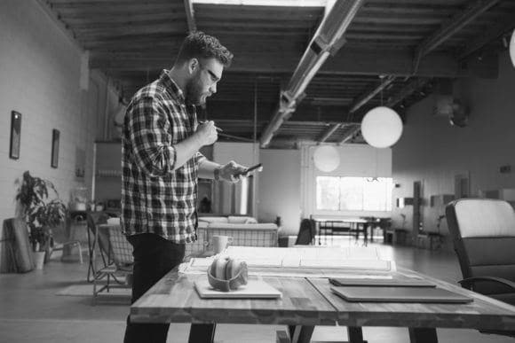 Architect standing at design table, looking at phone.