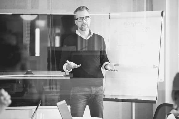 An information technology manager stands in front of his team and discusses an upcoming project.