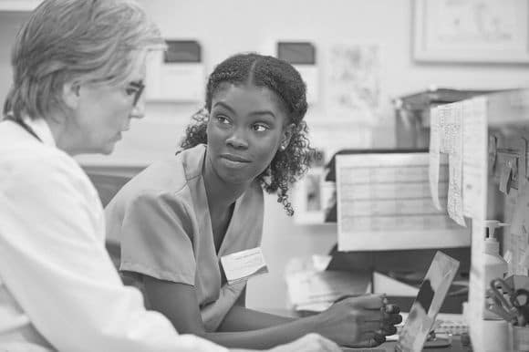 Medical assistant listening to a physician as she schedules appointments for a patient.