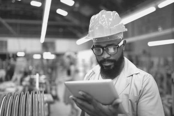 Quality assurance officer, wearing a hardhat and checking a tablet computer, doing his daily rounds at the factory.