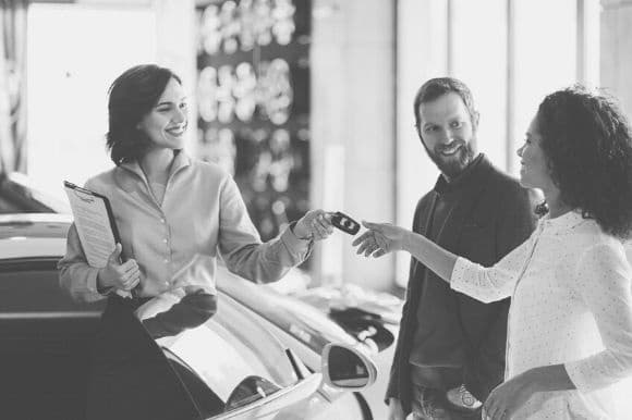 A car salesperson hands the keys over to a happy couple.