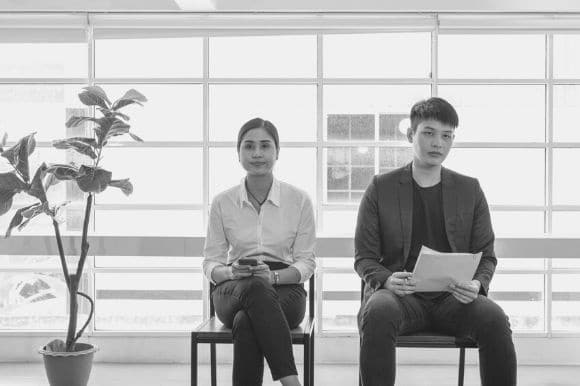 Candidates for open position, sitting outside of the interview room and holding their resumes.