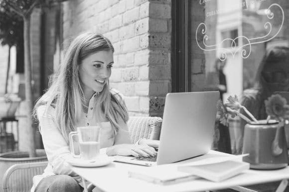 Small business owner sitting outside of a coffee shop, working on her small business blog.