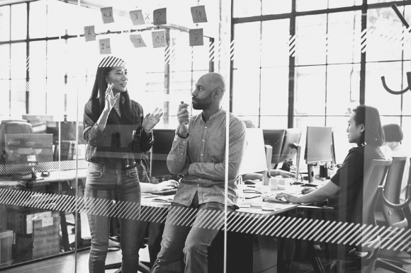 Two coworkers at the edge of a desk, brainstorming, and showing positive employee morale.