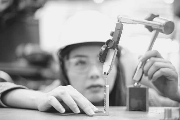 Assistant engineer, in a hard hat and protective eye gear, measuring a component.