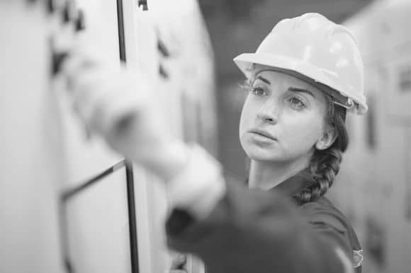 An electrical engineer, wearing a hardhat, checks an electrical connection.