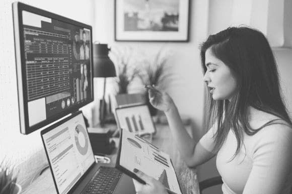 A financial analyst sitting at her desk and viewing multiple screens with financial data and graphs.