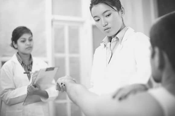 Physical therapy aide taking notes while her supervisor works with a patient.