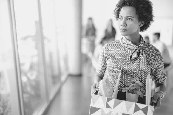 A woman carries her box of stuff out of the office after quitting her job.