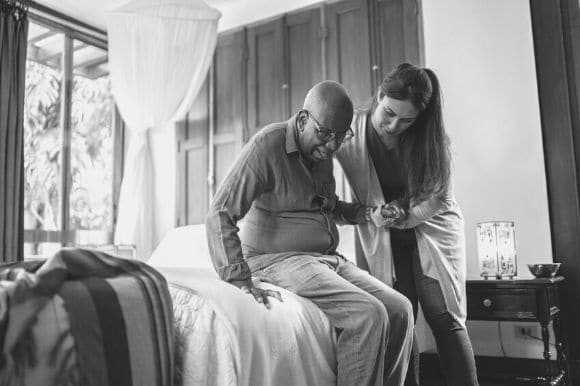 A home health aide helping an elderly man get out of bed.