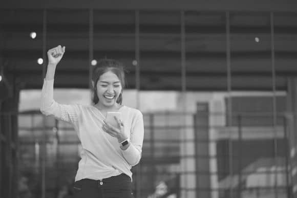 A happy job seekers pumps her fist after reading an encouraging message on her phone, illustrating the reach of mobile marketing recruitment.