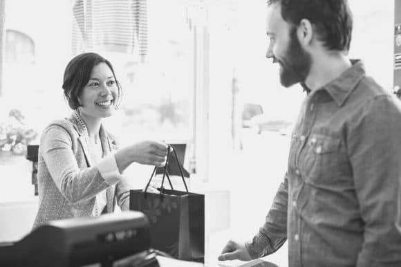 A retail employee helps out a customer and hands him a shopping bag.