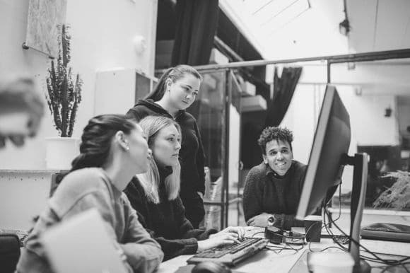 Four IT workers sitting around a computer, working out a problem together.