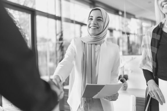 A supervisor, with clipboard, shaking the hand of one of her employees.