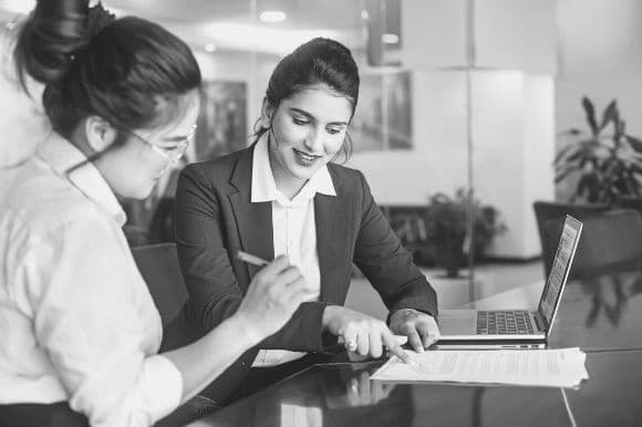 A law clerk helps a client sign legal documents at a table.