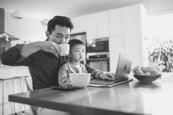 An employee with a flexible work schedule sipping coffee and checking email while holding a toddler.