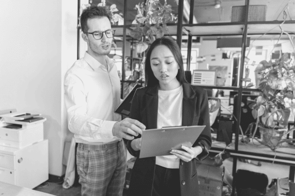 Two business managers looking at a clipboard and discussing whether they can afford the cost of hiring an employee.