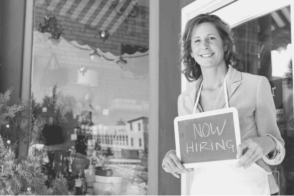Woman holding up a hiring sign outside of a restaurant