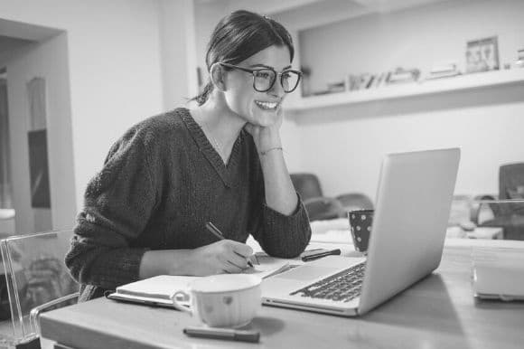 A woman at her kitchen table, smiling as she searches for jobs online.