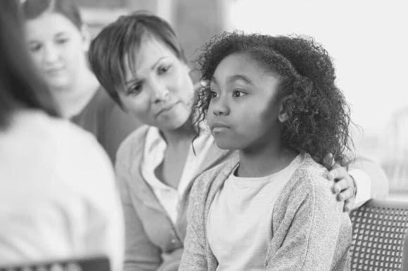 A school counselor comforts a young student.