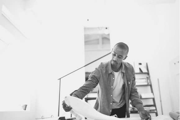 Architect working at his desk, unrolling a blueprint.