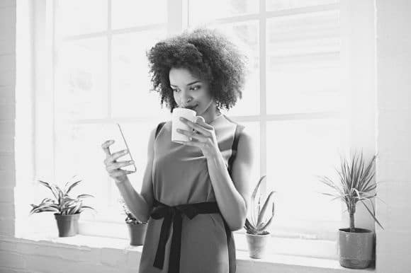A social media manager sipping coffee and checking her company's social media accounts on her phone.