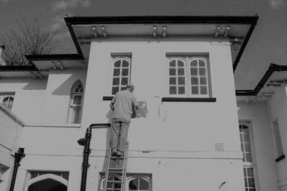 Man on ladder painting house.