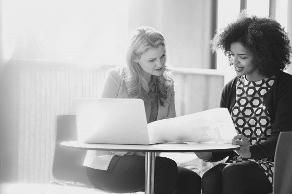 Manager meeting with her colleague, looking at papers and a laptop screen