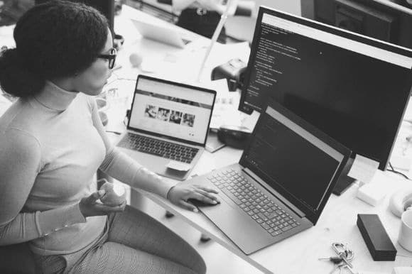 Web developer at her desk, checking code and eating an apple.