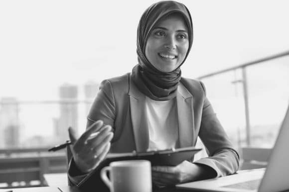 Woman in a business suit and hijab leading a business meeting.