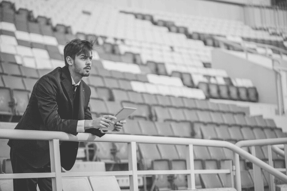 Athletic director leaning on the railing at a college stadium, looking out onto the field.