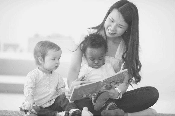 Babysitter sitting on the floor reading to two toddlers.