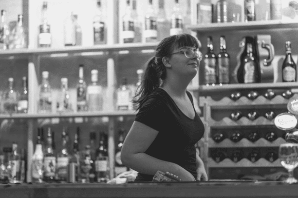Bar manager standing and smiling behind the bar.