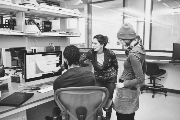 Computer scientist pointing at the screen and talking through an issue with coworkers.