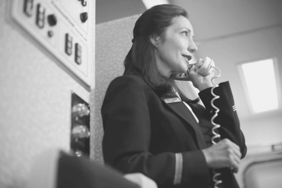 Flight attendant addressing passengers on the plane's intercom system.