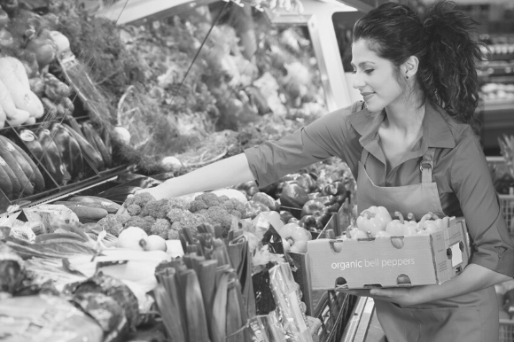 Grocery clerk with a box of bell peppers, restocking the produce bins.