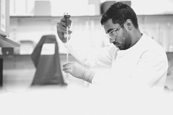 Industrial engineer in a white lab coat and goggles, measuring a substance with a graduated pipette.