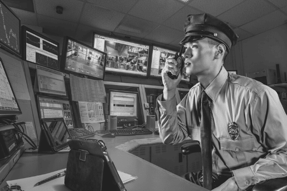 Security guard talking on radio and watching monitors from surveillance cameras.