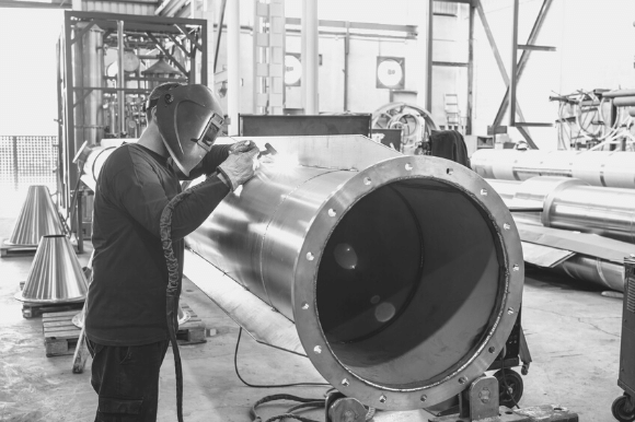 Boilermaker wearing a face shield and welding a large pipe together.