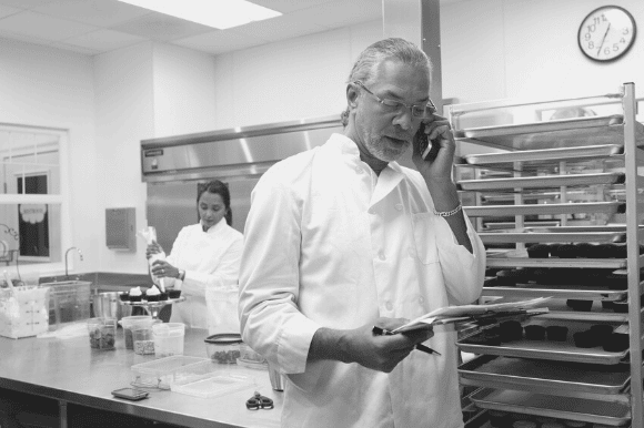 Executive chef on the telephone, restocking the kitchen, with a member of the kitchen staff working in the background.