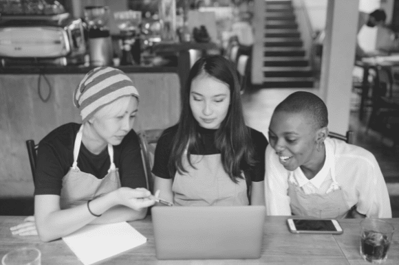 Business owner and two colleagues gathered around a laptop computer and discussing strategies for small business growth.