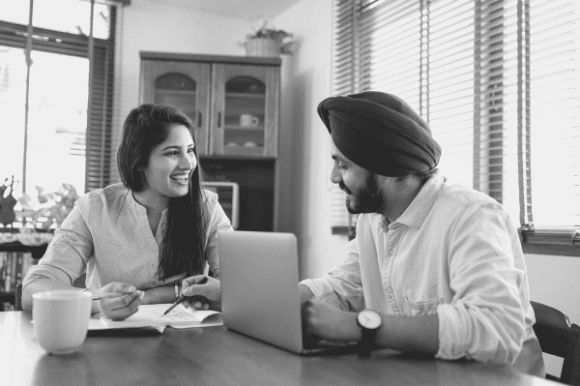 A man with a laptop is telling his friend about an opening at his company, an example of word of mouth recruitment.