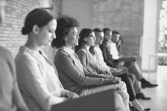 Job candidates participating in a mass hiring event at a company, sitting in chairs while awaiting their interviews.