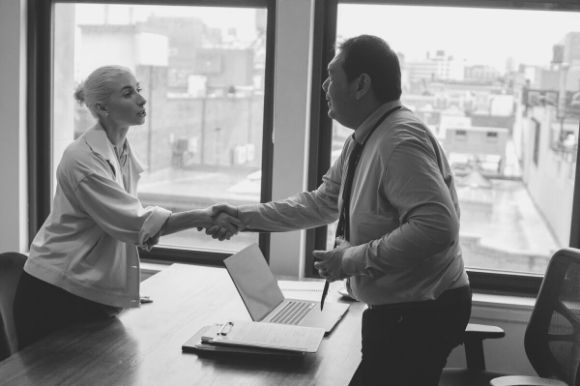 Manager shaking the hand of a boomerang employee who is returning to the office after a successful interview.