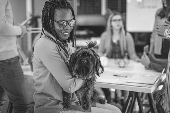 Woman, smiling, holding her dog. Office pets can be a good idea for your workplace, but not always.