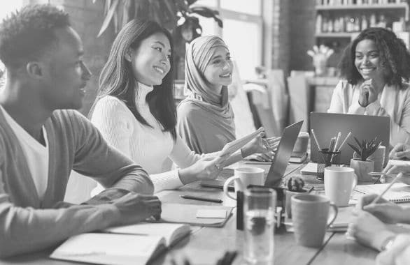 A diverse workforce gathering around a work station, talking and smiling.