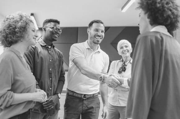 A man shaking another person's hand while attending a happy hour, just one type of creative recruitment strategy that works.