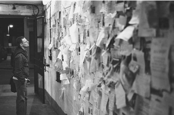 A job seeker standing next to a large kiosk/wall, looking at help wanted ads.